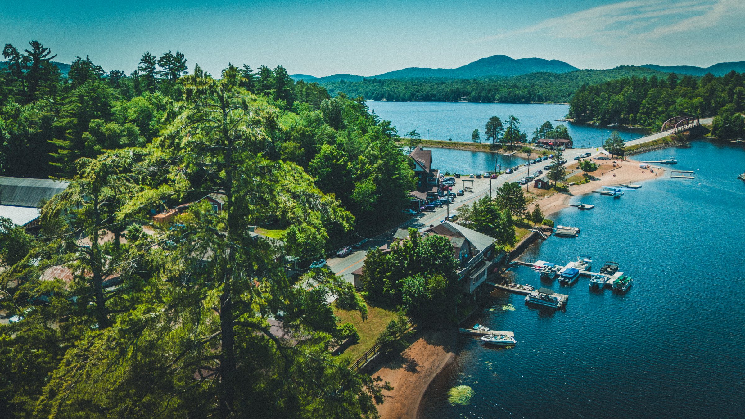 Aerial over Long Lake in the Adirondacks, with docks, a beach and mountains beyond